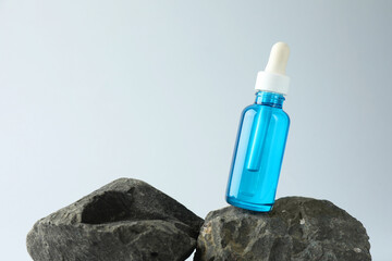 Bottle of cosmetic serum on stone against light grey background