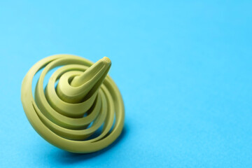 One green spinning top on light blue background, closeup. Space for text