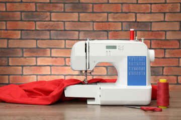Sewing machine with fabric and craft accessories on wooden table against brick wall