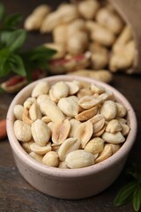 Fresh peeled peanuts in bowl on wooden table, closeup