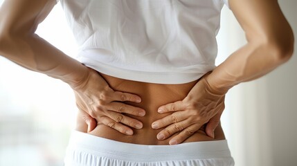 Women holding lower back in pain with clinical white backdrop.