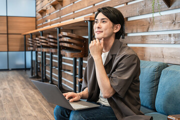 カフェ・喫茶店のソファでノートパソコンを使う若いアジア人男性
