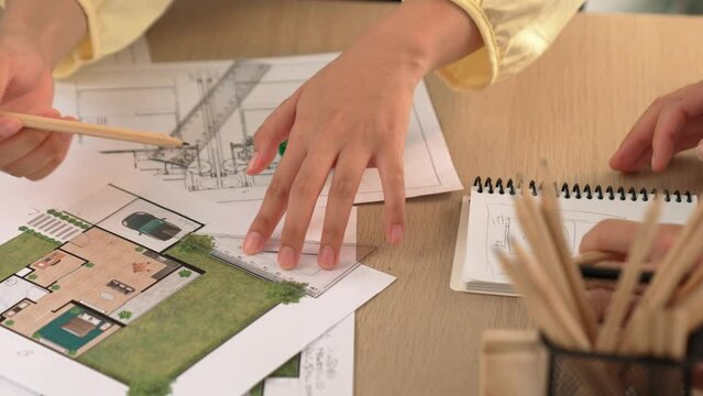 Architects using measurement tool and pencil tracing in building blueprint by coworker support on table with architectural document and wooden block scatter around at office. Closeup. Delineation.