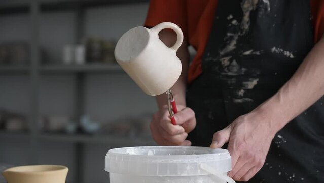 Close-up of a potter's hands glazing a ceramic mug. 