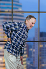 Aged mature man is having a back pain touching his back. Vertical shot of an old casual man suffering from backache.