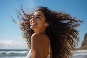 Naklejka premium A Latina Brazilian woman standing with her hair gathered by the seaside laughing summer smile.