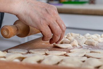 Woman hands are making a damp dumpling. On the wooden counter 