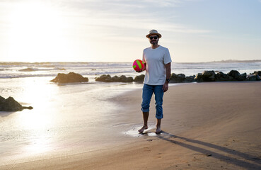 cheerful mature fit man walking on the beach holding a beach volleyball ball