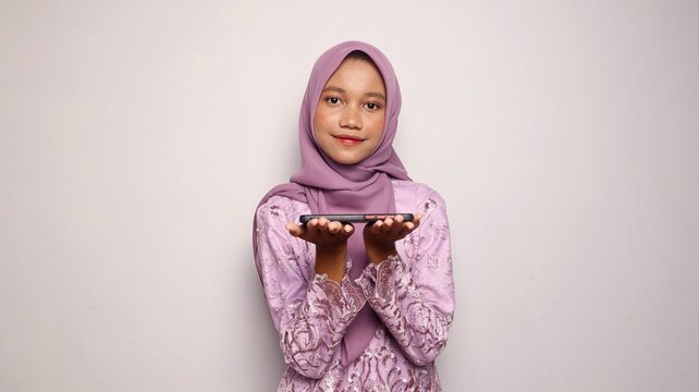 Portrait of a beautiful Indonesian teenage girl wearing a kebaya and hijab holding a smartphone