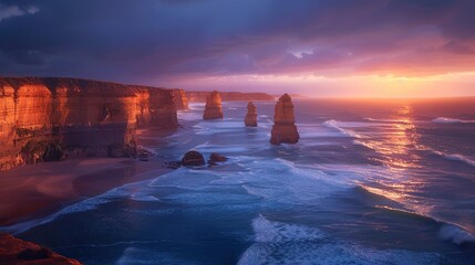 The image shows a beautiful sunset over the Twelve Apostles, a series of limestone stacks off the coast of Victoria, Australia. The sky is a vibrant mix of oranges, pinks, and purples, and the water i - obrazy, fototapety, plakaty
