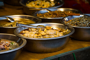 a variety of delicious foods displayed in metallic bowls at a street food stall