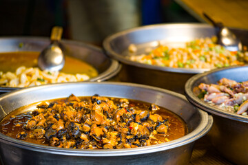 a variety of delicious foods displayed in metallic bowls at a street food stall