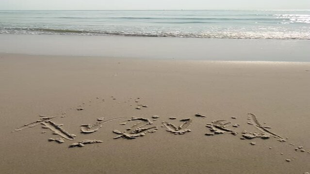 Sunrise up and waves roll in sandy beach, close up. Travel handwritten on wet sand of peaceful morning sea shore.