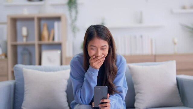 Happy young asian woman relaxing at home. Female smiling and talking chat with friend sitting on sofa and holding mobile smartphone. Girl using video call to close friend
