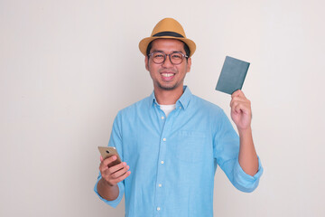 A man smiling at the camera while holding passport document and mobile phone