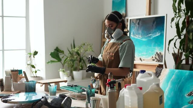 Resin art. Woman artist in respirator kneads mixing art epoxy resin in plastic cup working in art studio workshop. Female wearing protective gloves prepares resin by kneading it to desired consistency
