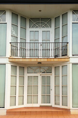 front entrance of a two story building house with floor to ceiling windows with curtains and balcony balustrade