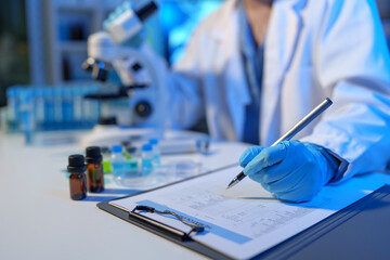 Asian scientist looking at a microscopic sample of experimental cyan is doing an in vitro vaccine experiment in a science lab. medical research concept.