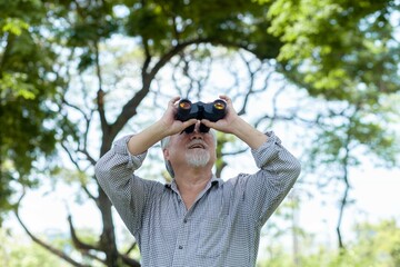 A man is looking through binoculars at something in the distance. The scene is peaceful and serene, with trees and a clear blue sky in the background. The man is enjoying the moment