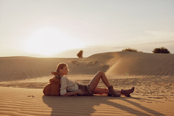 Woman sitting on top of sand dune enjoying sunset view, back to the sun