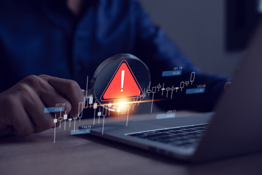 Businessman uses laptop with virtual warning sign to caution in investing, warning of economic situation, investment risk.