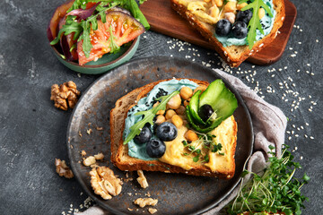 Vegetarian toasts with hummus, blueberry, avocado, tomato. delicious vegan breakfast on dark...