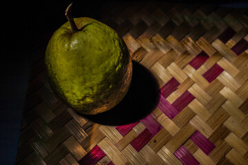 guava fruit isolated on woven bamboo with natural lighting from sunlight, dark background for copy...