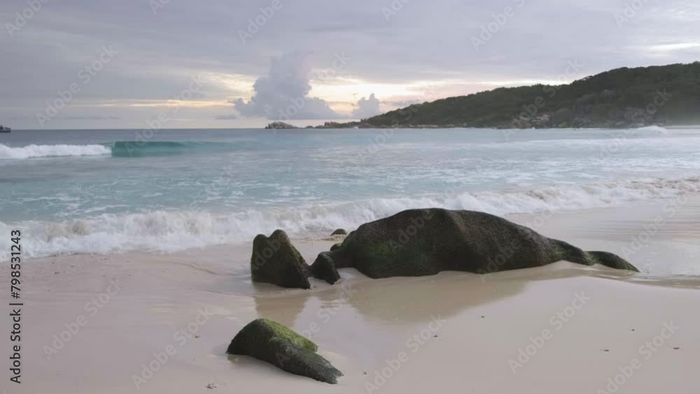 Poster a rocky beach with a large rock in the middle of the water. the sky is cloudy and the water is calm