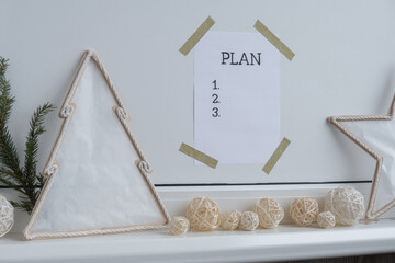 PLAN checklist text on paper note stick on while wall with cozy minimalistic handmade Christmas decor. New year aims resolutions. Low key festive Planning and setting goals concept