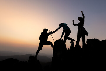Silhouette of person hikers climbing up mountain cliff and one of them giving helping hand. People...