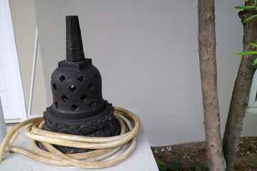 an artificial stupa made of cement. For outdoor decoration. black, with a water hose wrapped around...