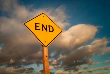 Yellow diamond shaped traffic sign with the word End written on it against a stormy cloudy sky