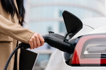 Close-up of a woman's hand charging an electric car at an outdoor charging station. Zero emission electric vehicle concept.