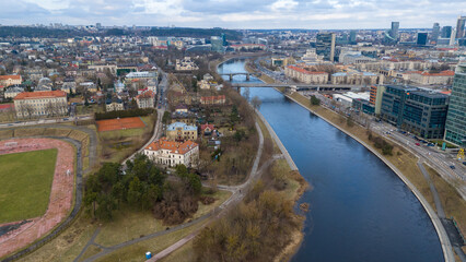 Fototapeta premium Drone photography of river shoreline going through city and people walking during spring day