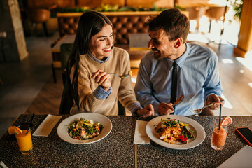 Happy young woman eating lunch with her boyfriend in a restaurant
