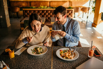 Happy young woman eating lunch with her boyfriend in a restaurant