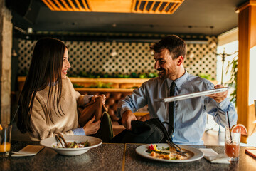 Two business people packing a laptop and leaving after a delicious meal in the restaurant