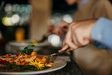 Close-up image of peoples hands cutting a dish while they having lunch at a restaurant
