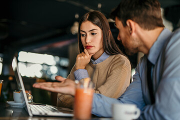 Shot of two people having a coffee at a coffee shop with a laptop in front of them