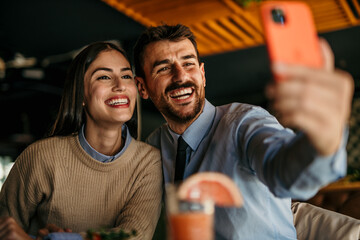 Happy couple eating lunch together in a restaurant and taking a selfie