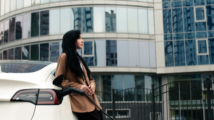 A businesswoman waits for her electric car to charge in the parking lot of a business center....