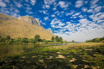 The background presents a landscape with a blue sky, towering mountains, and a winding river.