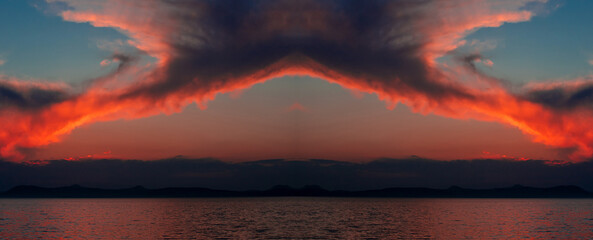 Amazing landscape with red clouds on the blue sky over the lake seen in the mirror. Mirror image of clouds with impressive shapes in the evening