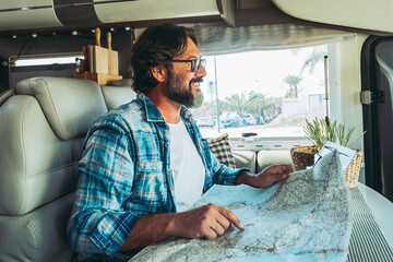 Happy mature man smilng inside a camper camping car using paper map guide to plan destinations...
