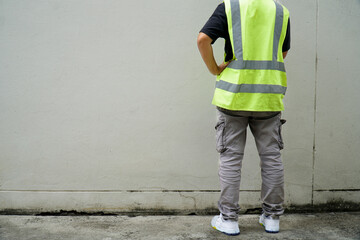 A man wearing a green reflective vest and cargo pants is standing with his hands on his hips in...