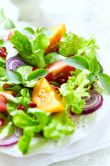 Salad with red and yellow Tomatoes and Pomegranate Seeds on bright wooden Background. Close up.