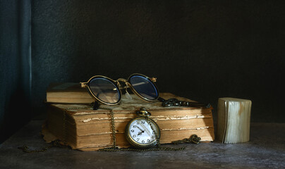 Still life with a pocket watch, glasses and old books.