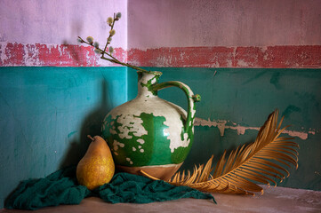 An old, peeling ceramic jug, a ripe pear and a dried palm branch.