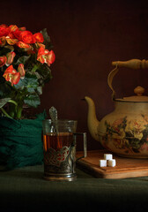 Obraz na płótnie Canvas Hot, aromatic tea in a glass with a glass holder, an old teapot and a blooming begonia.