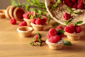 Tartlets with fresh raspberries and mint on a wooden table.